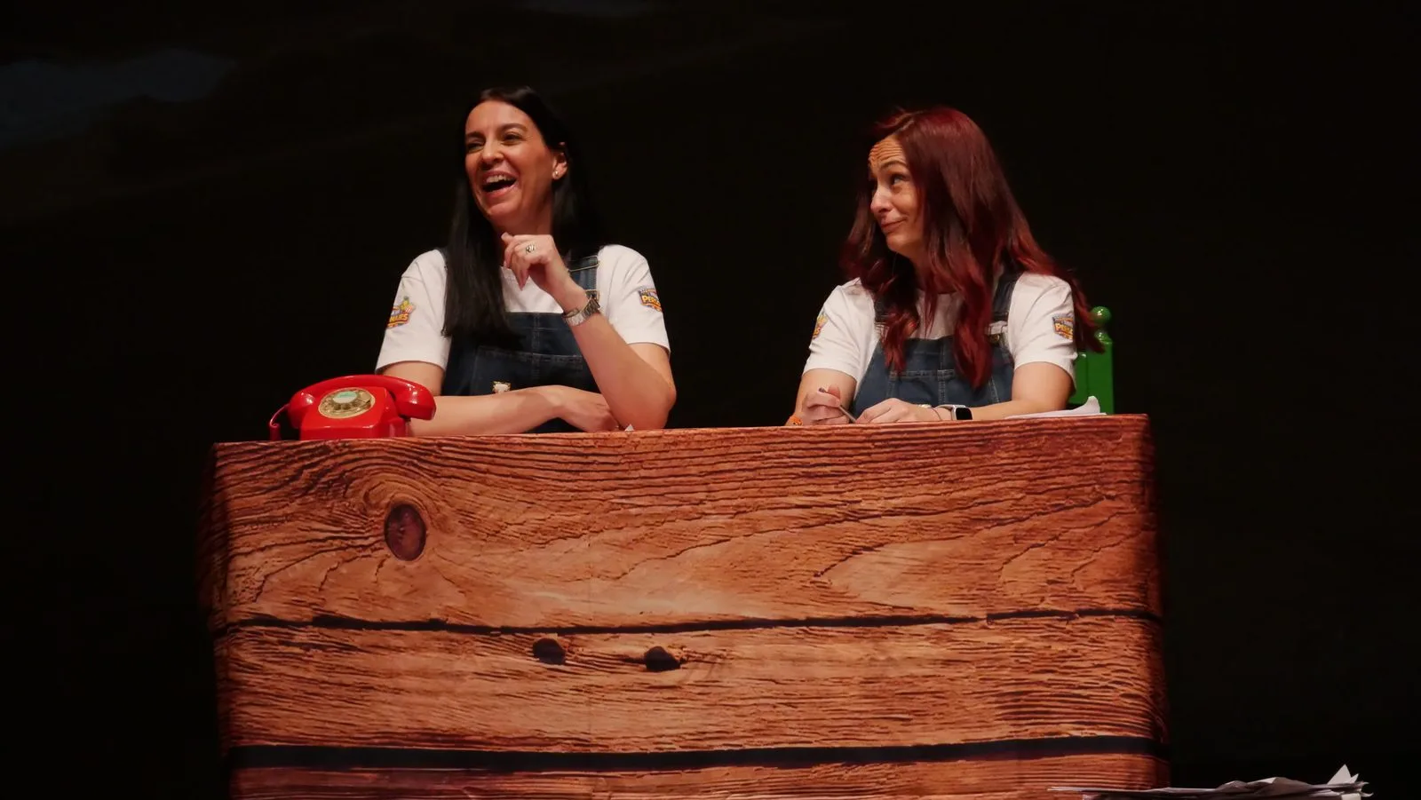 Tere y Lourdes, con el peto vaquero de Tilly y Lou, ríen sentadas tras un mostrador de madera en el escenario